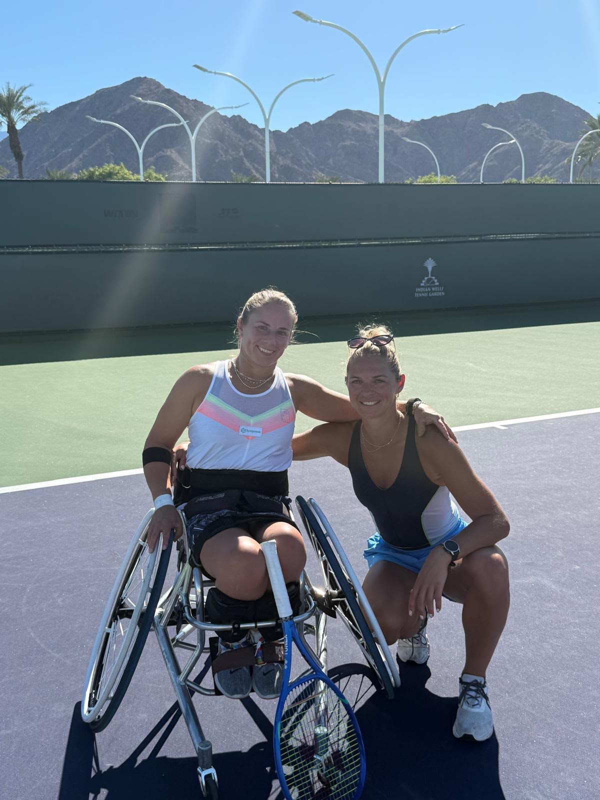 Two tennis players together on court, including a wheelchair tennis player